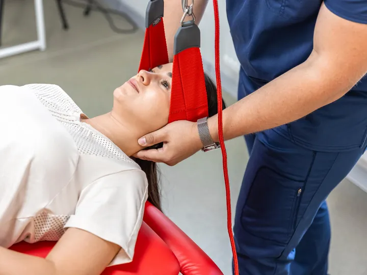 Fisioterapeuta apoiando a cabeça de uma paciente deitada durante uma sessão de tração cervical