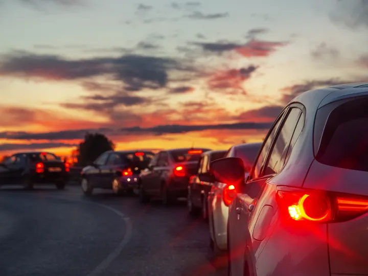 Fila de carros com as lanternas acesas numa estrada ao entardecer