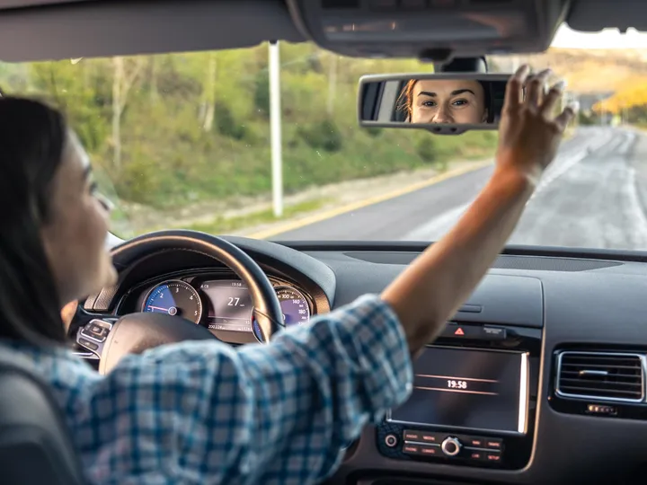 Motorista sorrindo pelo retrovisor enquanto ajusta o espelho
