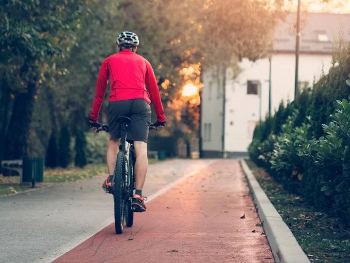 Ciclista de camisa vermelha pedalando numa ciclovia arborizada ao entardecer