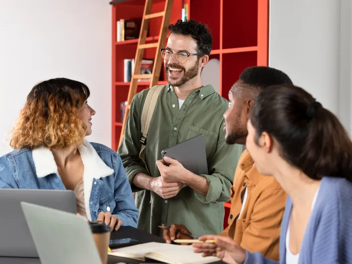 Grupo jovem conversando animado em volta de uma mesa com notebooks