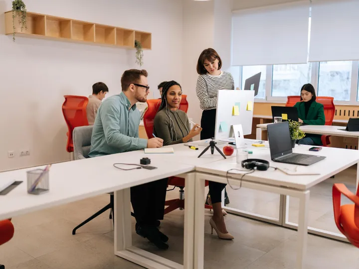 Jovem no escritório revisando um trabalho no computador com dois colegas