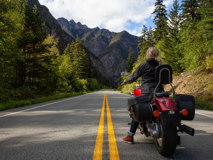 Motociclista parada numa estrada entre montanhas, olhando o caminho