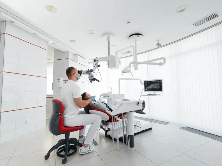 Dentista examinando um paciente com microscópio, em consultório claro