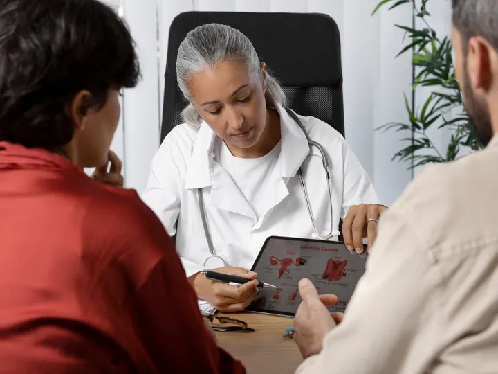 Médica explicando um exame no tablet a um casal, durante a consulta