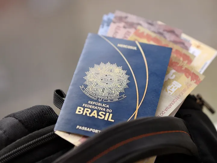 Passaporte brasileiro e notas de real saindo do bolso de uma mochila